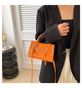 Detail of bright orange PU leather crossbody bag with long tassels and metal zippers