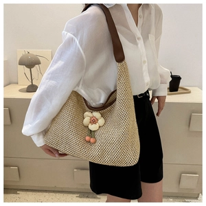 Detail of hand-woven straw tote bag with beige 3D floral accent and brown shoulder strap