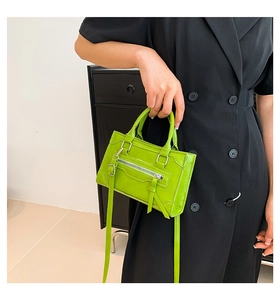 Detail of a grass green leather mini handbag with long fringe tassel and metal zipper accent