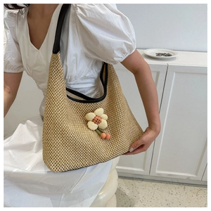 Detail view of woven straw shoulder bag featuring a large decorative 3D floral accent