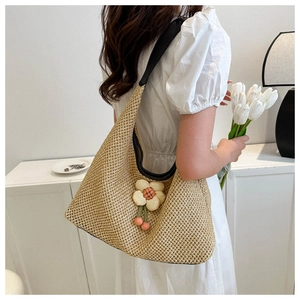 Detail of beige woven tote bag featuring floral charm and black leather shoulder strap