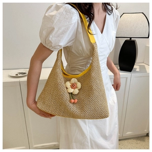 Detail of straw woven hobo bag with yellow shoulder strap and floral cherry charms