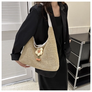 Detail of woven straw shoulder bag with decorative cream flower charm and white trim