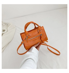 Close-up of orange faux leather handbag with decorative zippers and fringe details