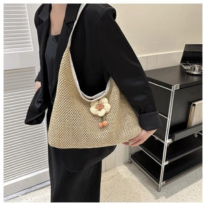 Detail of hand-woven straw hobo bag featuring a cream floral charm and knit texture