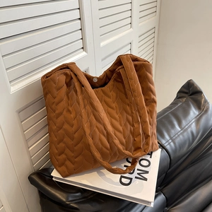 Caramel brown quilted tote bag with braided texture and magnetic closure on leather sofa