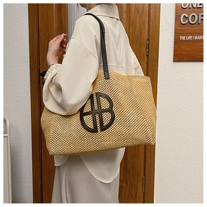 Detail of a straw tote bag with brown leather HB letter logo and matching shoulder straps