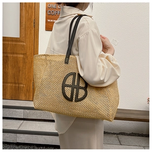 Detail of hand-woven straw tote bag featuring a large leather logo and black shoulder straps