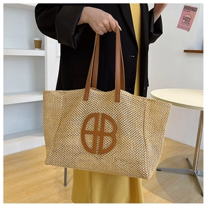 Detailed macro view of the woven straw texture and brown leather HB logo on the tote bag