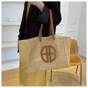 Detail of woven straw tote bag with brown leather logo patch and shoulder straps