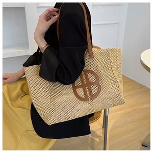 Detail of hand-woven summer tote bag with leather strap and decorative logo emblem