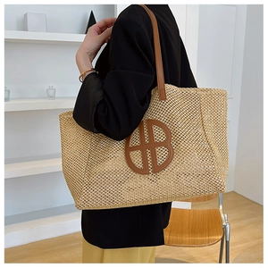 Large straw tote bag with leather HB logo patch shown on shoulder for daily summer style