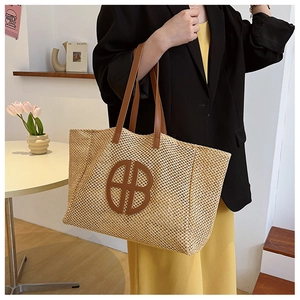 Detailed view of beige woven straw tote bag with round leather logo and brown straps
