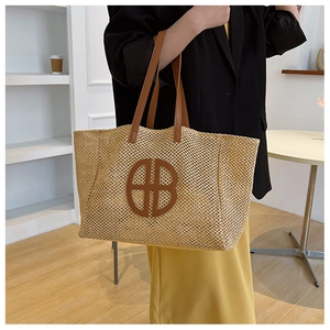 Detail of a woven straw tote bag with circular leather logo and brown shoulder straps