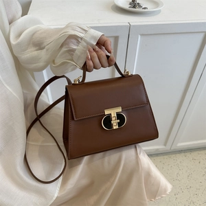 Brown PU leather crossbody handbag with golden T-lock shown in a minimalist home setting