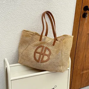 Fashionable straw tote bag with brown leather straps and logo in a cozy home setting