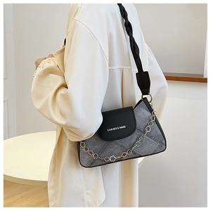 Detail of grey denim shoulder bag featuring a metal flower chain and black leather flap