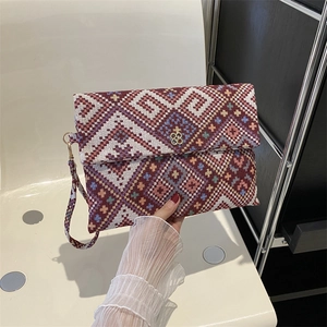 Detail of vintage woven clutch bag with red geometric patterns and gold clover buckle