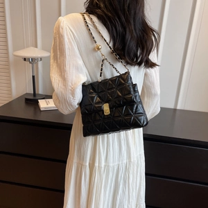 Modern black quilted chain bag with gold lock shown in minimalist lifestyle home setting