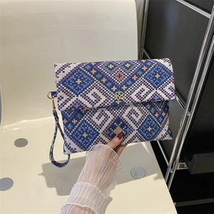 Detail of blue and white geometric jacquard envelope clutch with golden floral clasp