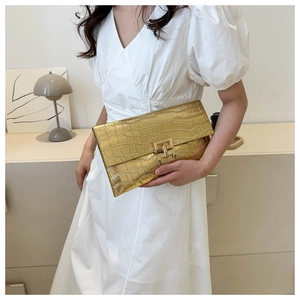 Dettaglio di una pochette dorata con texture coccodrillo e una fibbia in metallo centrale
