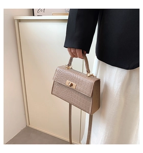 Close-up of beige crocodile texture handbag with gold rotating metal lock and handle