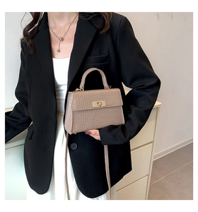 Detail of khaki crocodile pattern square bag with gold twist lock on black blazer