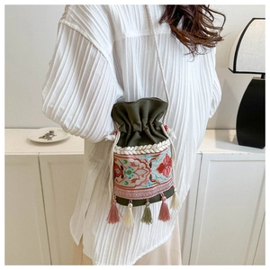 Close-up of ethnic bucket bag with floral embroidery and colorful tassels on green canvas