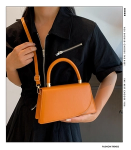 Detail of a bright orange crossbody bag with a geometric flap and metal ring handle