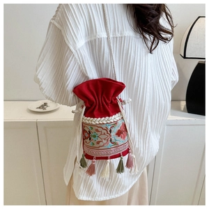 Detailed close-up of ethnic floral embroidery and colorful tassels on a red bucket bag