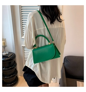 Borsa a mano in pelle verde con patta curva indossata da una modella in interni