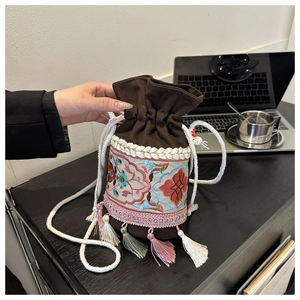 Detailed close-up of ethnic embroidery and colorful tassels on a brown canvas bucket bag