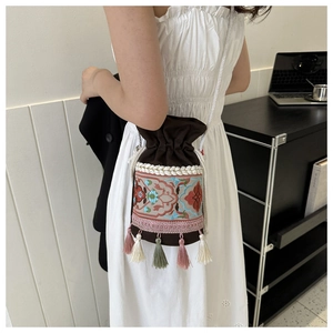 Close-up of ethnic floral embroidery and colorful tassels on a brown bucket bag