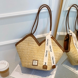 Straw woven tote bag with brown leather handles and decorative ribbon on a book