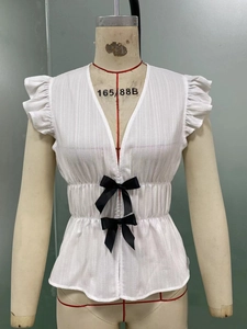 Detail der weißen Kurzarmbluse mit V-Ausschnitt und schwarzen Satin-Schleifen-Dekorationen