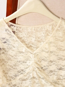 Detailed view of beige lace top featuring delicate floral patterns and V-neck design