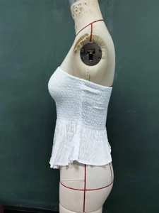 Detailed side view of white smocked tube top with peplum hem on dress form