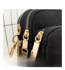 Detail of black nylon crossbody bag featuring triple gold zippers and twill texture