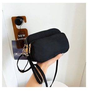 Detail of a black nylon crossbody bag with three golden zippers and adjustable strap