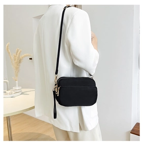 Detail of black nylon crossbody bag with gold zippers worn with white blazer
