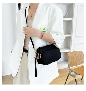 Model wearing a black water-resistant nylon crossbody bag with gold zippers and pockets