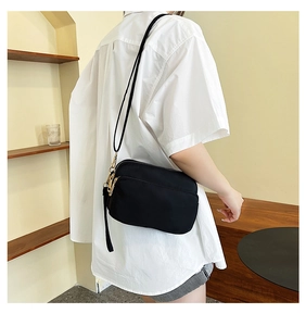 Close-up of lightweight black nylon crossbody bag with gold zippers worn by a model