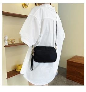Detail of a black nylon crossbody bag on a model wearing an oversized white shirt