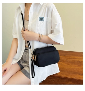Detail of black nylon crossbody bag with multi-layer zippers and dual strap design