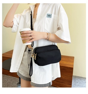 Detail of waterproof black nylon crossbody bag featuring multi-pocket design and gold zippers