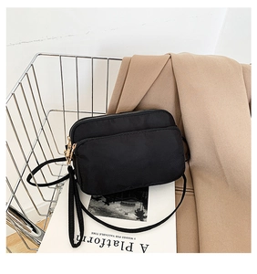 Detail of black waterproof nylon crossbody bag with gold zippers in a styled setting