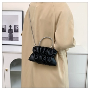 Detail of black pleated cloud bag with silver rhinestone handle on beige trench coat