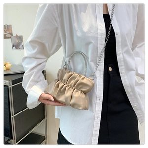 Detail of a beige ruched handbag with a sparkling rhinestone handle and silver chain strap