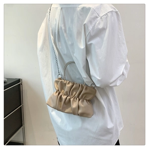 Detail of elegant beige pleated cloud bag with rhinestone handle and silver chain strap