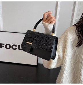Detail of black handbag with sequin top, matte leather base, and golden metal handle hardware